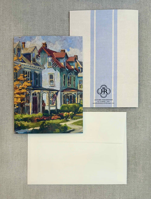 A stationery set laid flat on a textured gray fabric background, featuring a printed card with a painted house illustration, a white envelope, and a white card with pale blue vertical stripes and a small monogram logo.