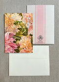 A floral greeting card with large pink and cream flowers, shown with a white envelope and a white postcard featuring pink vertical stripes and a small 'JR' monogram.
