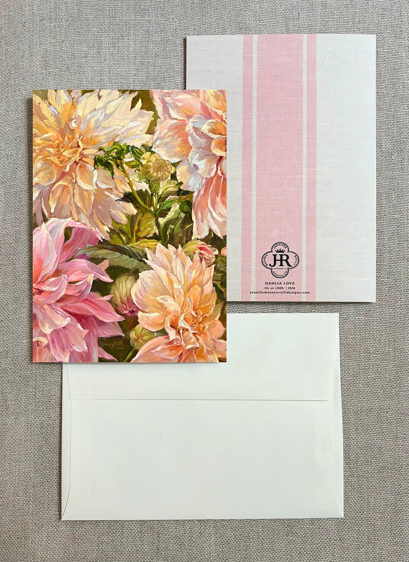 A floral greeting card with large pink and cream flowers, shown with a white envelope and a white postcard featuring pink vertical stripes and a small 'JR' monogram.