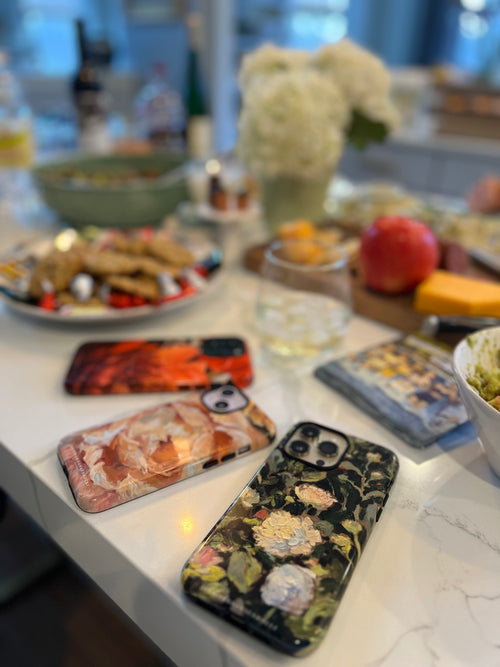 Three phone cases on a table with a blurred background of food and decor