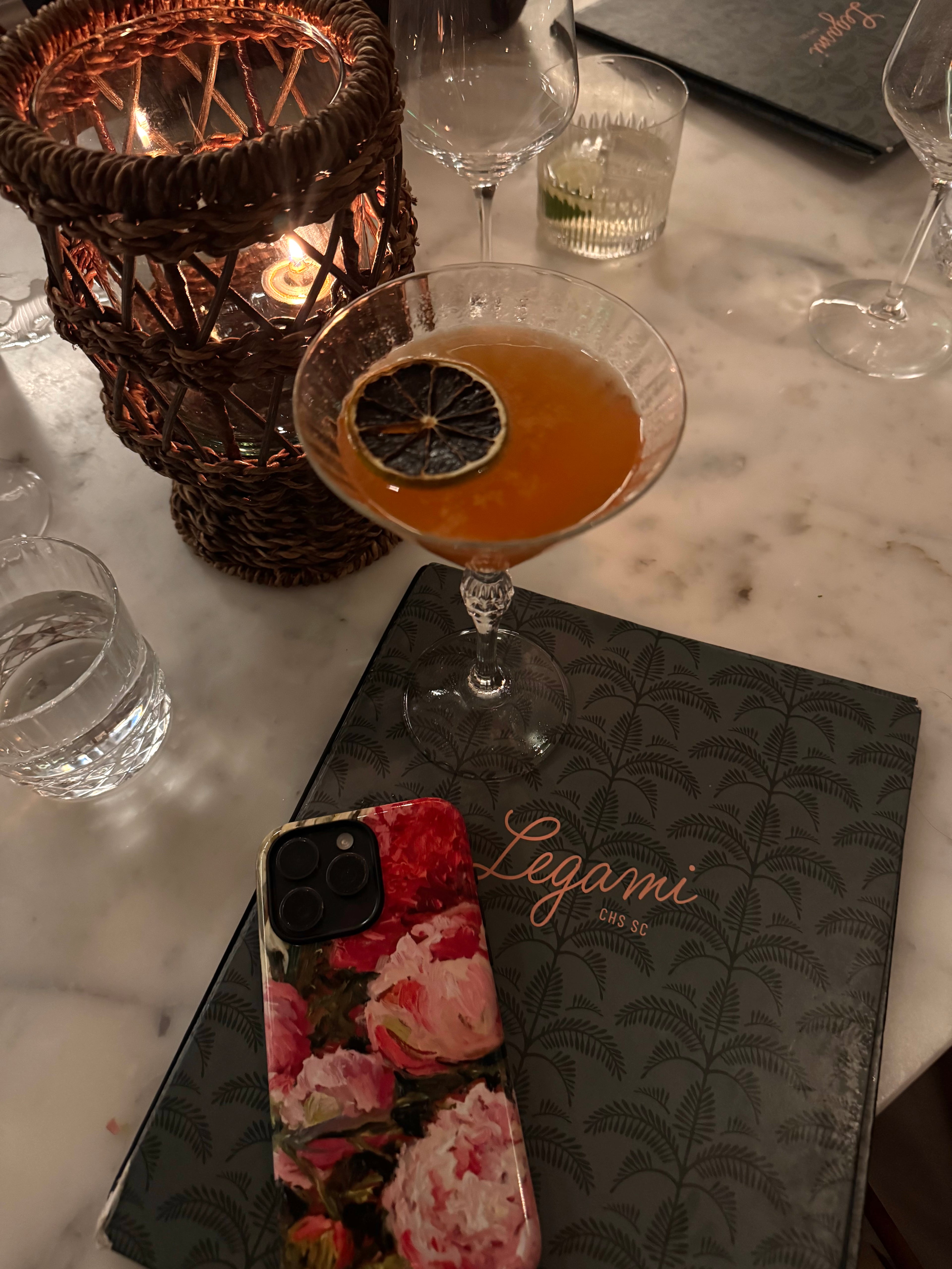 Cocktail with a lemon twist on a marble table with a 'Legami' menu and J'Adore phone case