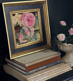 Framed floral painting on a stack of books with a vase of flowers in the background