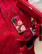 Red high-heeled shoes with a floral phone case on a red textured surface.