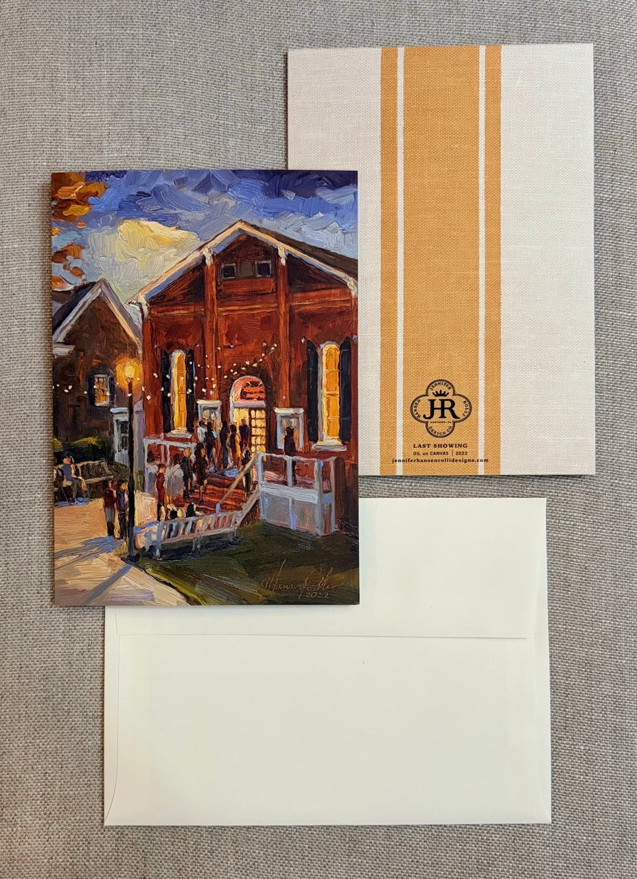 A stationery set laid flat on a textured gray fabric background, including a printed card with an impressionistic painting of a building exterior at dusk, a white envelope, and a white card with two vertical gold stripes and a small monogram logo.