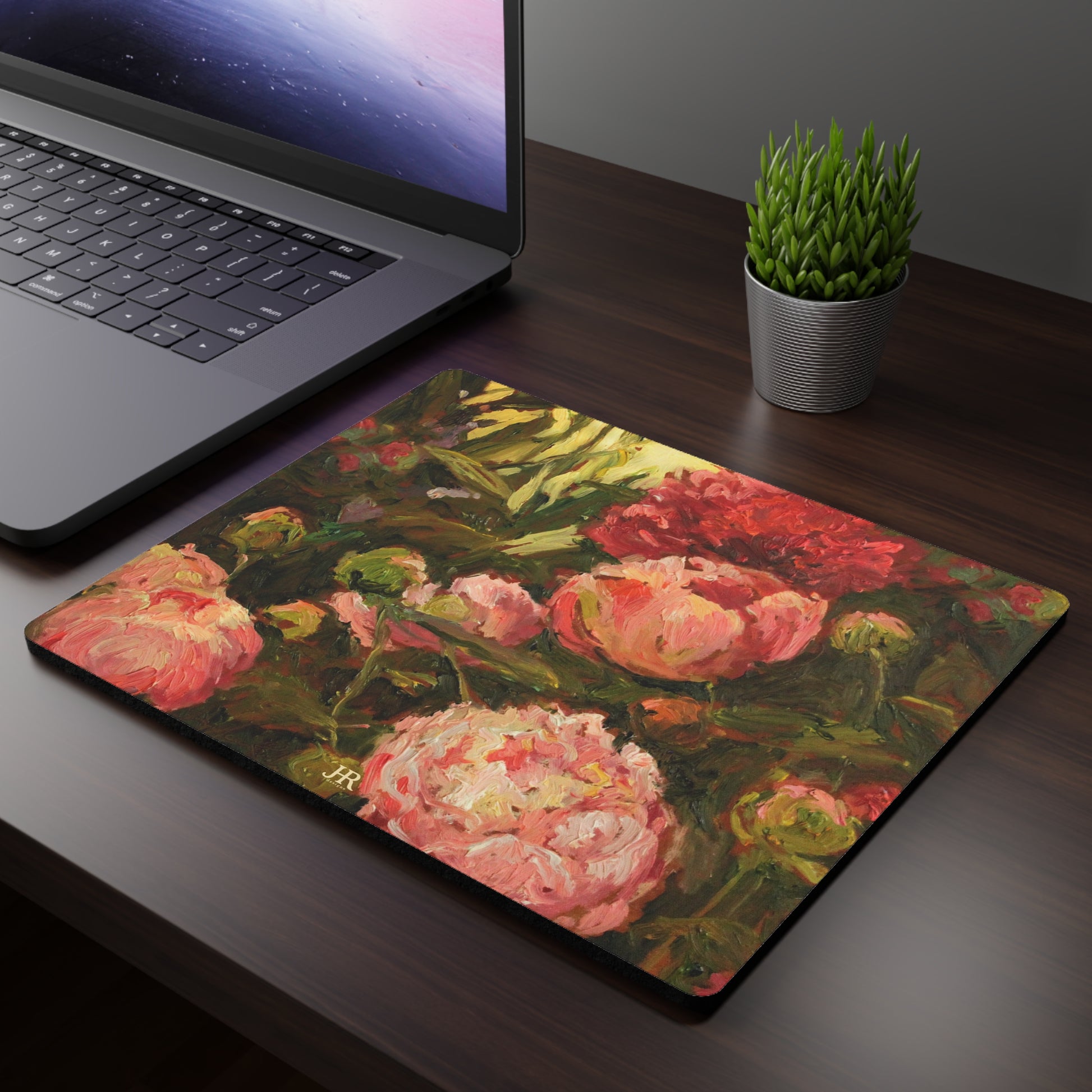 A mousepad shown on a desk featuring the pink peony artwork of artist Jennifer Hansen Rolli.