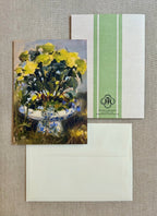 A floral greeting card featuring an impressionist painting of yellow and blue flowers, shown with its matching cream envelope and a white envelope with green vertical stripes and a monogram logo.