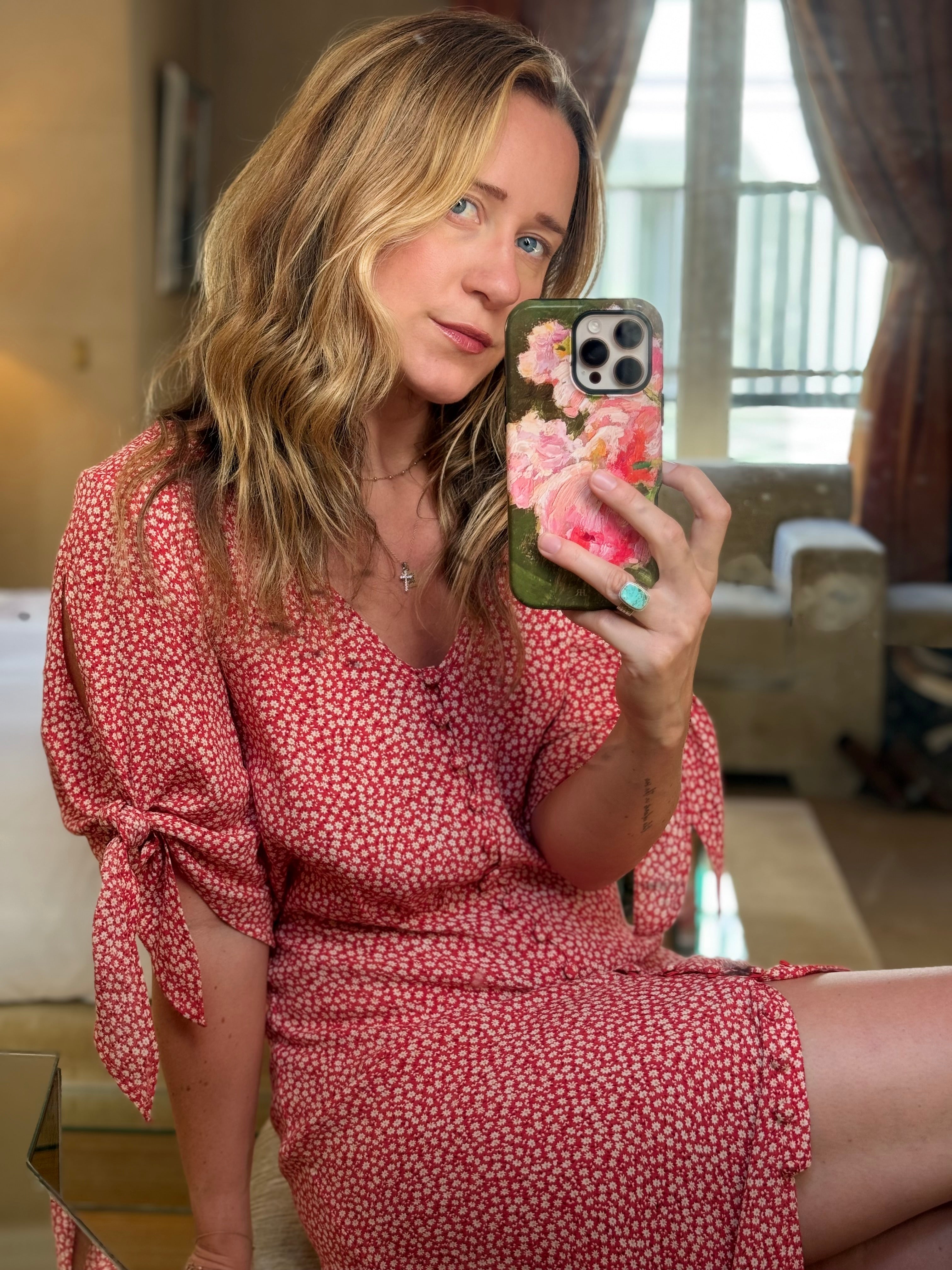 Woman in a red floral dress taking a mirror selfie with a phone case featuring flowers.
